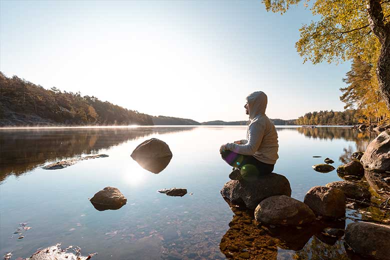 Mann sitzt auf einem Stein am See