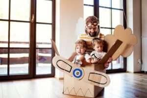 Papa spielt mit Kindern in einem Flugzeug aus Karton