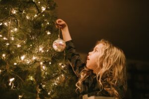 kleines Kind hängt Kugel an Christbaum