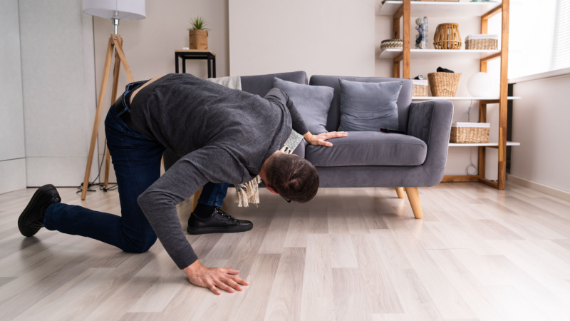 Mann fertig für die Arbeit angezogen sucht seinen Schlüssel unter dem Sofa. Ist das wohl eine gute Ausrede, um nicht oder zu spät zur Arbeit zu kommen?