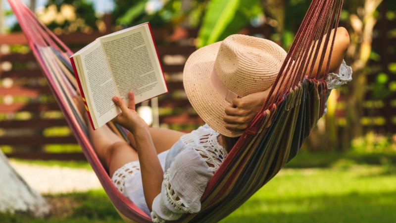 Eine junge Frau entspannt in der Hängematte und liest ein Buch.