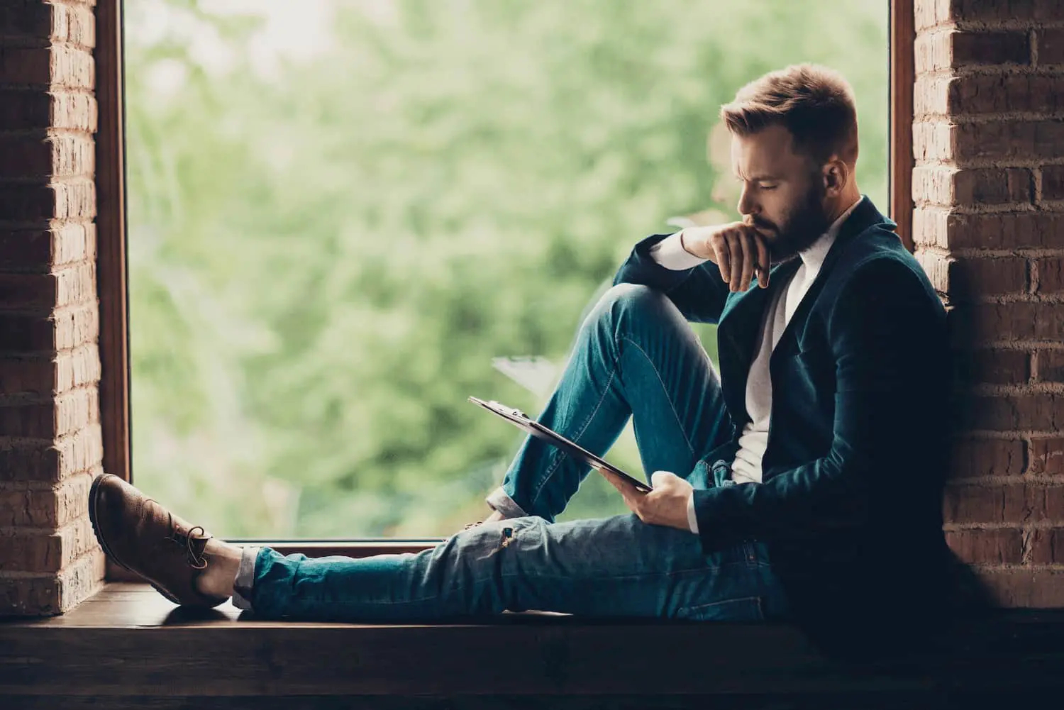 CEO in Jacke und Jeans, sitzt auf der Fensterbank