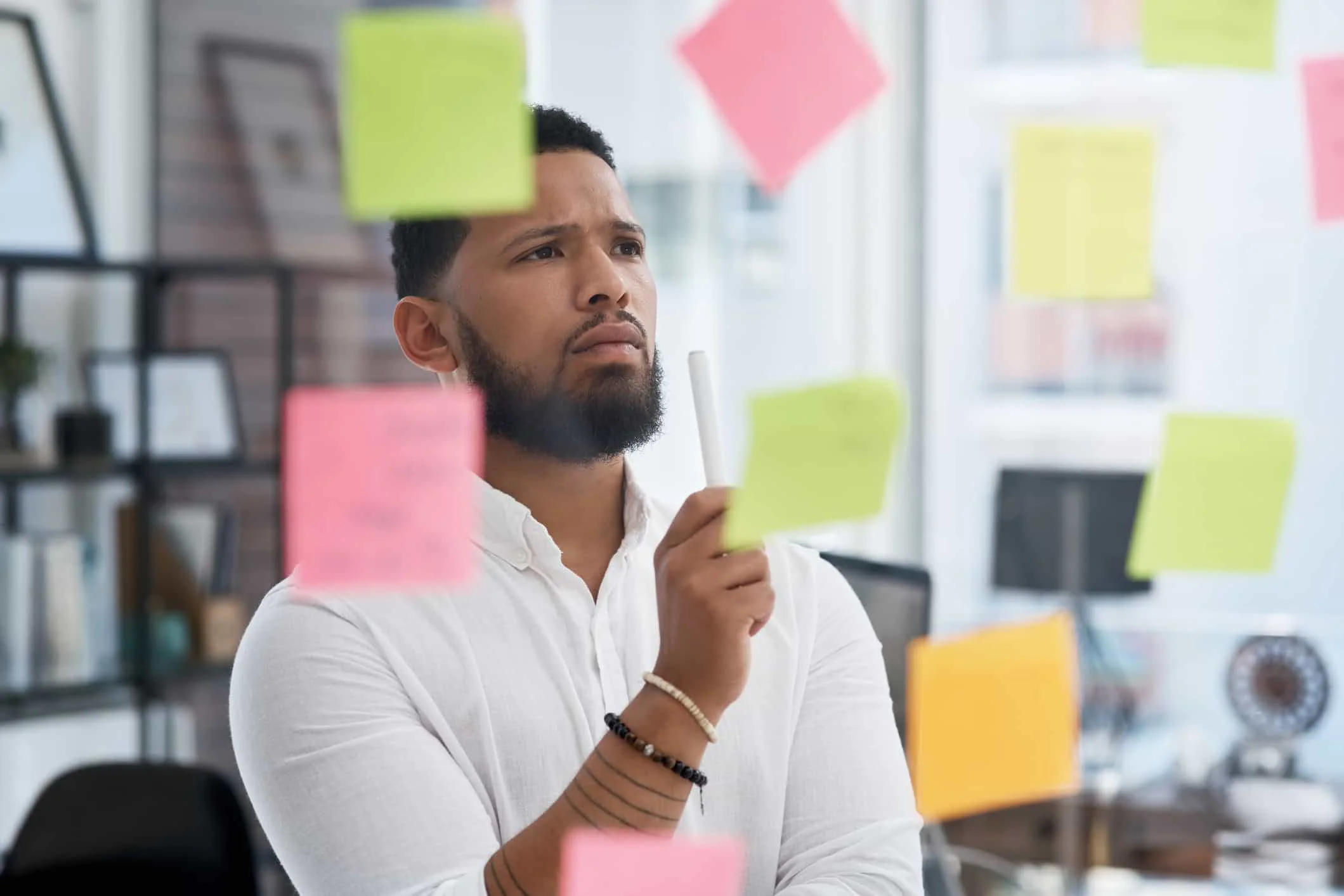 Mann grübelt vor Glaswand mit Post-Its