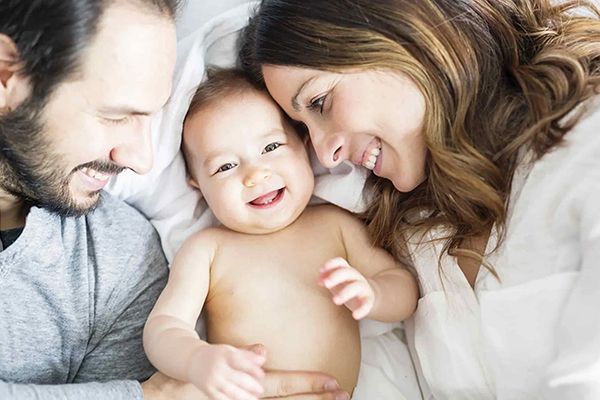 Vater und Mutter kuscheln mit Baby im Bett