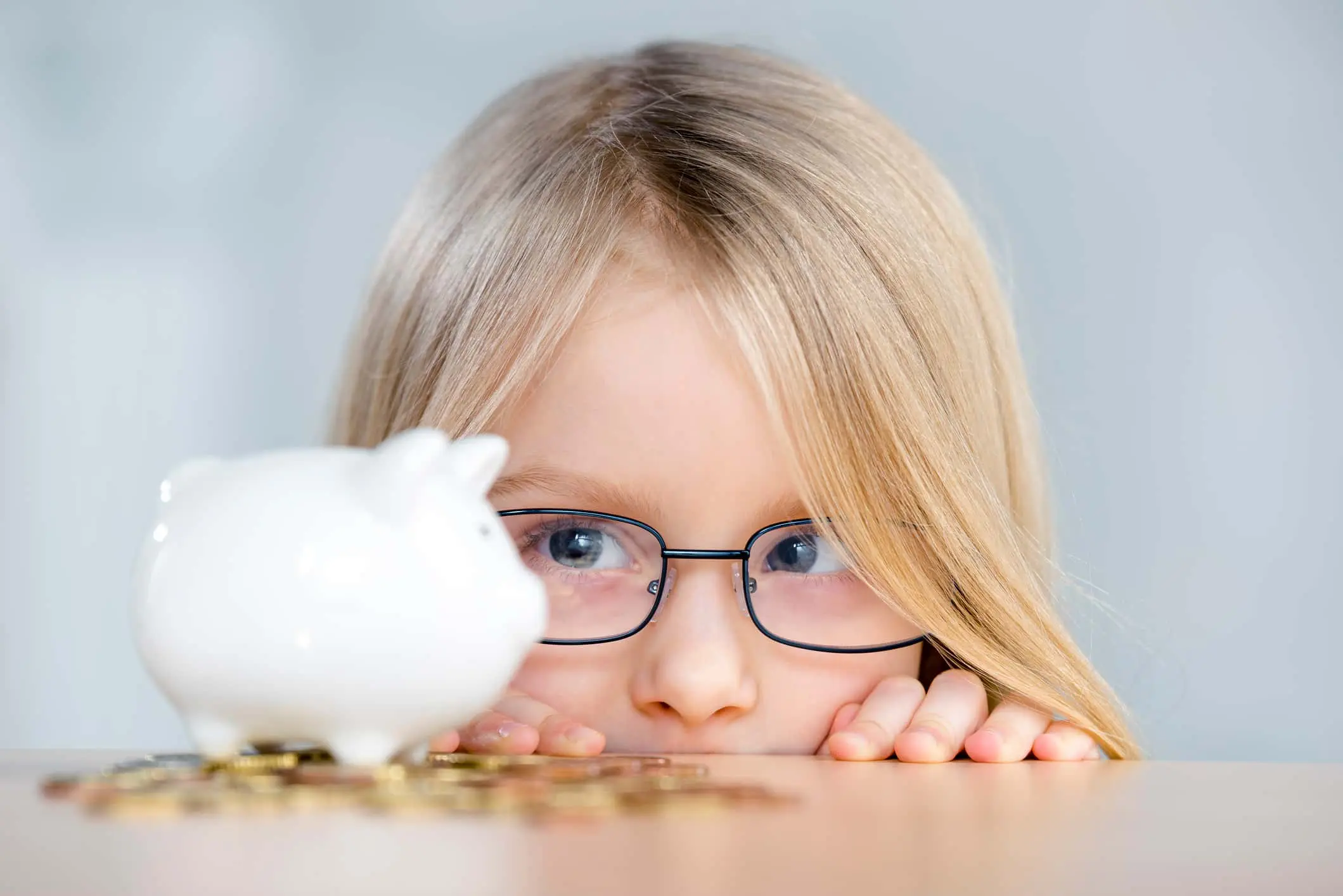 Mädchen mit Brille schaut auf ein Sparschwein